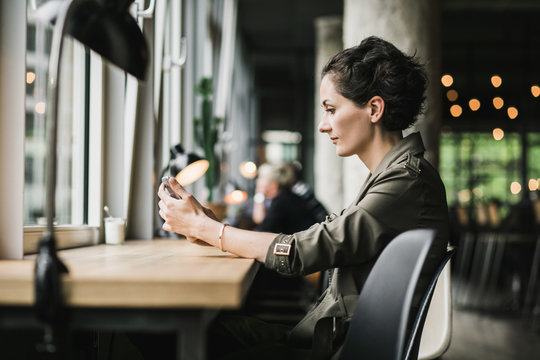 Short dark haired woman sitting in a cafe waiting