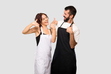 Couple of cooks giving a thumbs up gesture and smiling because has had success on grey background