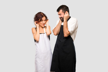 Couple of cooks covering ears with hands. Frustrated expression on grey background