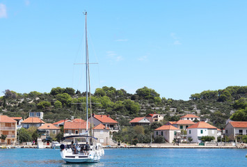 Fototapeta na wymiar Kaprije, Croatia, Europe - 7 9 2018: Embankment of a small Croatian town in the Adriatic Sea. Sailing yacht on the background of the Dalmatian Riviera. Tourism and architecture of the Mediterranean. 