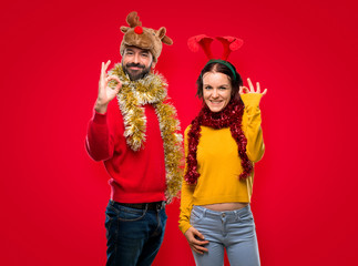 Couple dressed up for the christmas holidays showing an ok sign with fingers on isolated red background