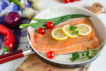 Fresh salmon in a pan with lemon and cherry tomatoes ready to cooking.