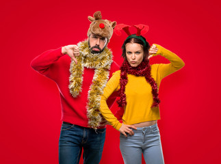 Couple dressed up for the christmas holidays showing thumb down sign with negative expression on isolated red background