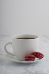 2 chocolate french macarons with a cup of coffee on a white marble table.