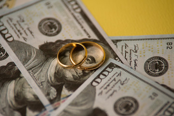 Golden wedding rings on dollars bill background. Divorce or infidelity concept