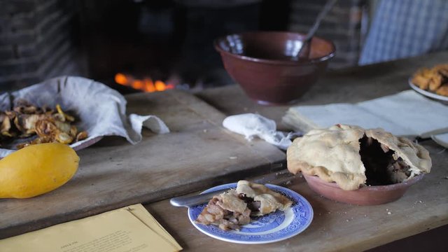 Rustic table in a traditional farmhouse kitchen with freshly baked apple pie and open fireplace in the background.