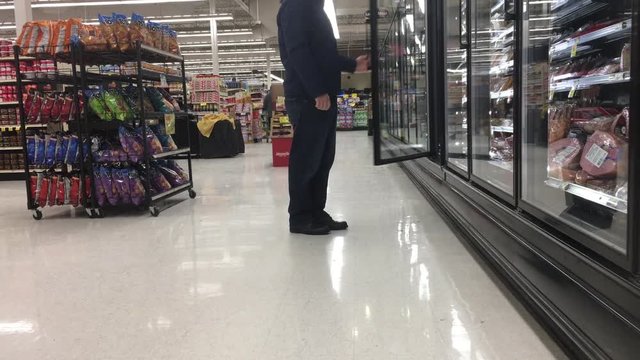 Man opens freezer door in cold section of grocery store and grabs several items before walking away.