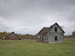 Fototapeta na wymiar Dreary Abandoned Dilapidated Farm House and Barn with cloud skies in northern Minnesota