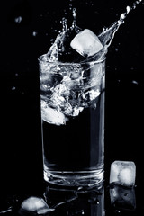 Water splash isolated. Water splash in glass with ice cubes and spilled water isolated on black background. Health concept.