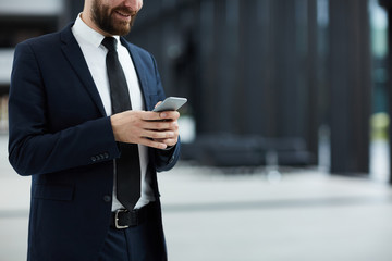 Elegant businessman messaging in smartphone while standing inside modern building