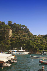 Obraz premium PORTOFINO, ITALY - suggestive view of Portofino harbor with an antique tower among lush Mediterranean vegetation and the boats moored