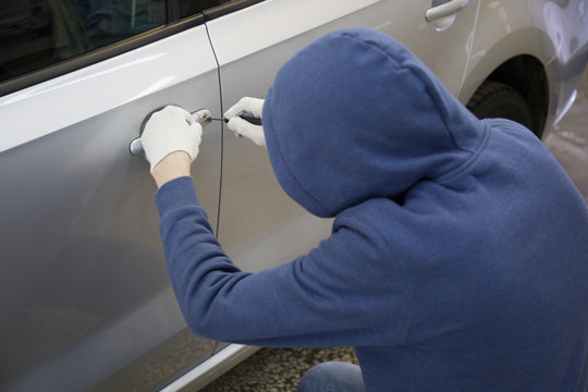 The hijacker tries to break into the car with a lock pick. Car thief, car theft.