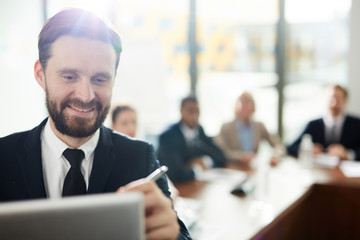 Young bearded man making financial report or presentation to audience by whiteboard in conference hall