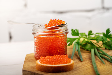 caviar appetizer - jar with red roe and herbs on the table
