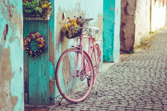 Pink vintage bike with basket full of flowers next to an old cyan building in Spain