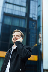 Happy young man talking by smartphone on background of modern business center