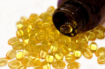 Yellow capsules omega 3 poured from dark pharmaceutical bottle. Gel pills and vial lying on white...