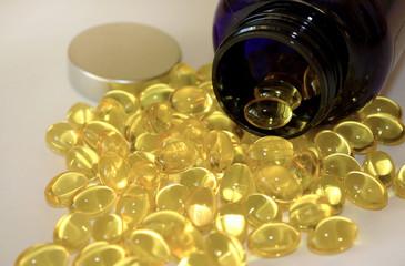 Yellow capsules omega 3 poured from dark pharmaceutical bottle. Gel pills and vial lying on white...