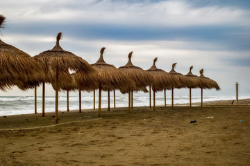 Straw beach umbrellas on the beach full of garbage in a stormy day