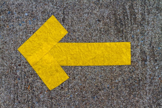 D.I.Y. yellow arrow symbol builds by pike leak seal tape shown on old concrete floor of the walk way. Textured background and copy space.