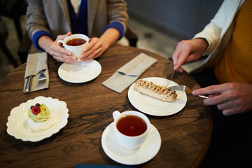 Young man cutting piece of appetizing cake on plate while having tea break with girlfriend in cafe