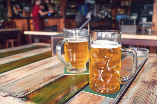 Glasses of light beer on pub background. Pint glass of golden beer with snacks and grill food on wooden table in pub, bar