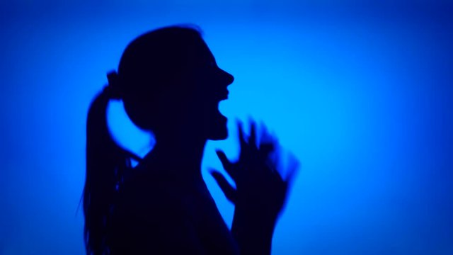 Silhouette of young frustrated woman crying. Female's face in profile screaming in despair on blue background. Black contour shadow of teenager's half-face showing strong negative emotions