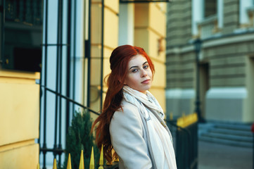 Portrait of a young beautiful red-haired girl in the autumn city . Woman wearing a coat and a green dress