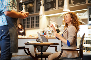 Young woman explaining to waiter which dessert she would like to have while sitting by table in cafe
