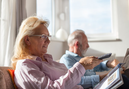 Elderly Couple Watching Tv And Reading Newspaper