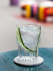 Gin tonic cocktail with ice and cucumber in a glass on a wooden table of a street cafe at a colorful blurry background