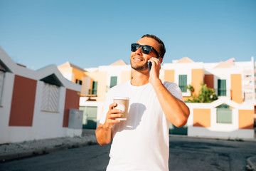 Happy young man talk on phone and drink coffee and walk on street