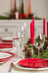 Merry Christmas and Happy New Year! Тable setting festive decor - white and red dishes, red candles in the candlesticks, juniper branches and fir cones.