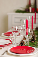 Merry Christmas and Happy New Year! Тable setting festive decor - white and red dishes, red candles in the candlesticks, juniper branches and fir cones.