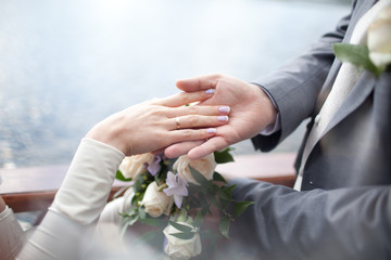 The bride's hand with a ring on the finger lies in the hand of the groom on the background of a bouquet of white roses