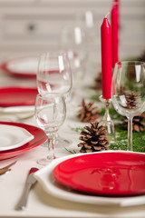 Merry Christmas and Happy New Year! Тable setting festive decor - white and red dishes, red candles in the candlesticks, juniper branches and fir cones.