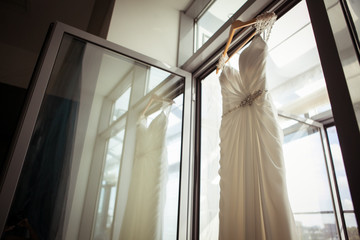 White wedding dress hanging on a hanger by the window