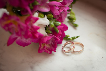 Two gold rings lie next to a purple bouquet on a marble table