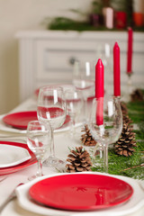 Merry Christmas and Happy New Year! Тable setting festive decor - white and red dishes, red candles in the candlesticks, juniper branches and fir cones.
