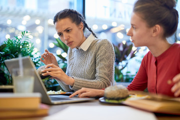 Obraz premium Confused girl showing her groupmate something on laptop screen during lunch in college cafe