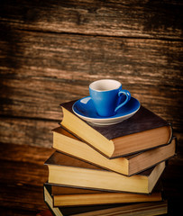 Blue cup of coffee and books on wooden table and background