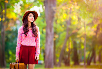 Beautiful brunet girl with suitcase in the park. Autumn season time.