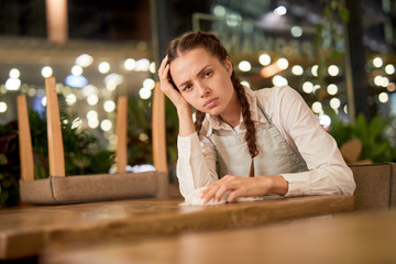 Young waitress with headache after hard working day sitting by table in cafe