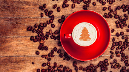 Cup of coffee with Chrismtas tree symbol and coffee beans on wooden table.