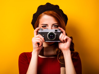 Redhead woman in beret with scarf and vintage camera on yellow background.