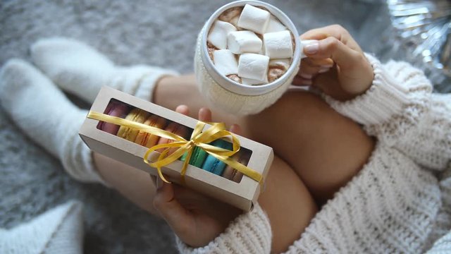 Fall Winter Cozy Concept. Woman Legs In Socks, Hot Cocoa Cup And Macaron Gift Box