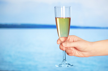 A glass of champagne in hand against the background of the sea. Close-up.