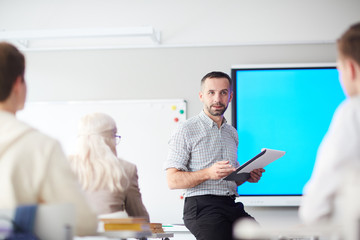 Confident teacher with document looking at group of students while explaining the main points of...