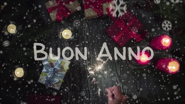 Animation Buon Anno - Happy New Year in italian, female hand holding a sparkler, falling snow. Top view