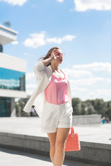 Fototapeta premium Woman on city background. Business woman on urban landscape wearing white jacket and shorts.